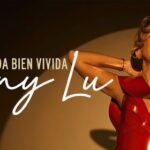 Mujer sonriente con vestido rojo bajo un reflector, promocionando el álbum “Una Vida Bien Vivida” de Fanny Lu