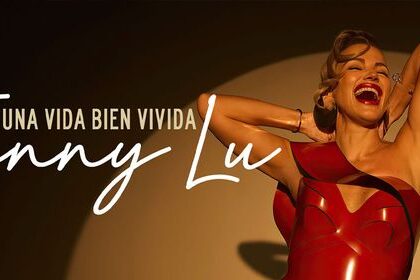 Mujer sonriente con vestido rojo bajo un reflector, promocionando el álbum “Una Vida Bien Vivida” de Fanny Lu